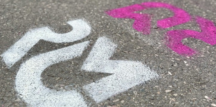 Ein asphaltierter Weg auf dem Campus Westend. Auf dem Asphalt sind die Buchstaben RMU für Rhein-Main-Universitäten in Weiß und Pink aufgedruckt.