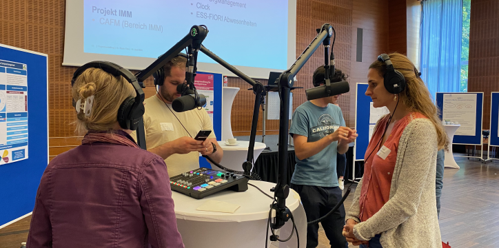 Aufgebautes Podcastset und Personen vor Mikrophonen, die eine Aufnahme auf der Digitalmesse machen.